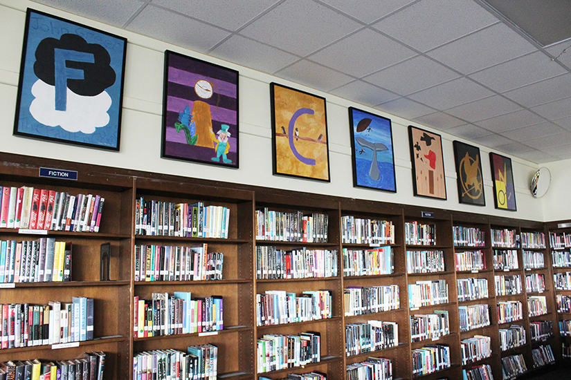 Wooden bookcases filled with books and paintings above them spelling out the word fiction.