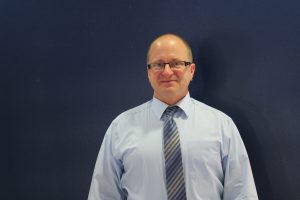 Chris Palmer wearing glasses in blue button down shirt and blue striped tie