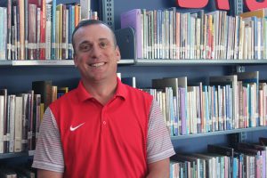 Man wearing red shirt smiling in front of shelves of books