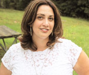 woman smiling; has white blouse on and shoulder length brown hair