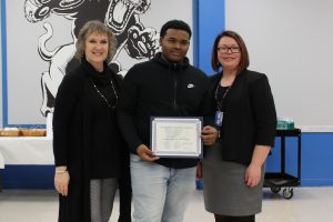 Krishna Foster stands between the Monticello Superintendent of Schools and Board of Education President and holds his Scholar Athlete certificate during the Board Award ceremony. 