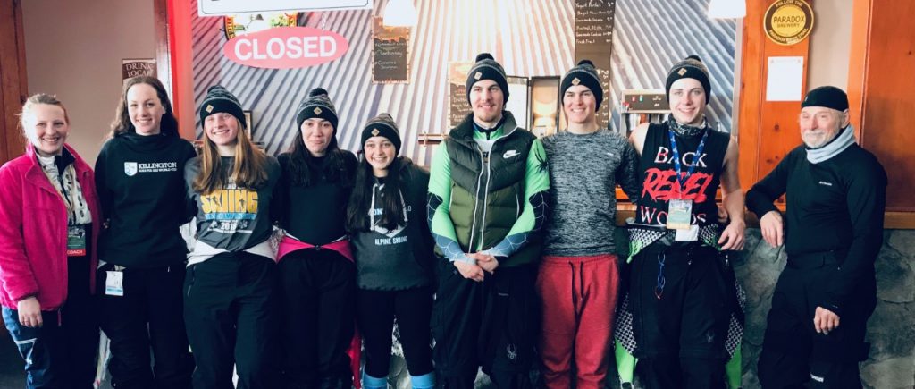 Seven high school ski team members, most with knit hats on, smile after the state tournament. On either side are their coaches.
