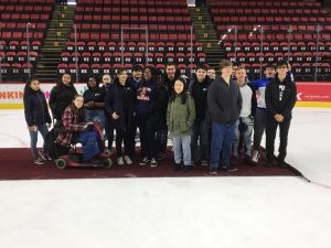 17 high school students stand on a carpet on the ice in an arena