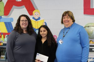 Two women flank fourth-grade student holding an envelope that contains her gift card