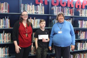 Two women flank a sixth-grader who holds an envelope with his gift card.