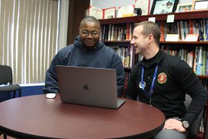 MHS Principal Stephen Wilder and student Tylan Williams are seated at a desk in front of a computer and looking at each other 
