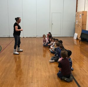 a teacher stands in front of a row of seated students and addresses them 