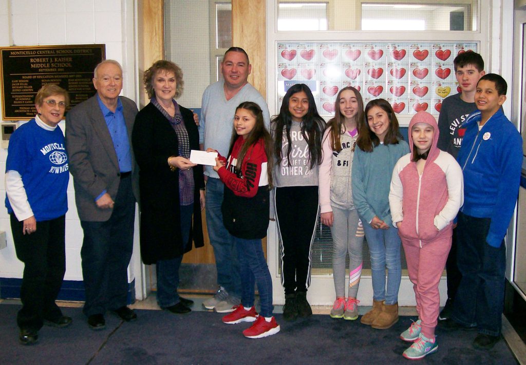 Four adults and seven middle school students in a row as one of the students presents a check to one of the adults