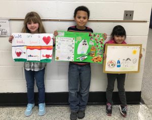 Chase students in grades K through 2 who won the poster contest stand in the hallway holding their winning work 