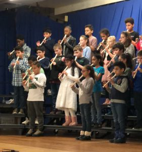 Large group of elementary students on risers on stage playing recorders