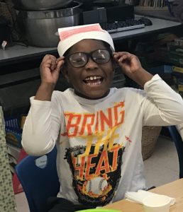 students sit at table eating plates of green eggs and ham and smiling