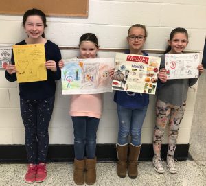 Four students are standing in a hallway and holding up the posters they created.