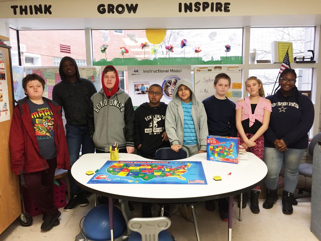 Eight middle school students surroud a table with the completed puzzle of the United States