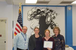 Christine Cavello stands flanked by staff members and holds her Board Award certificate 