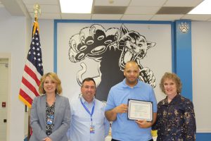 John Burkhalter stands, flanked by staff members, and holds his certificate during the Board Awards cerremony 