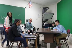 Gary Silverman sits around a table with a group of students during morning announcements