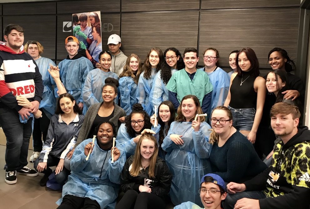 Approximately 20 students who went on the trip pose for a picture in their hospital gowns. Smiling