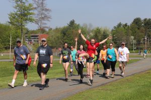 a group of runners racing during a 5k. One runner is jumping up in the air. 