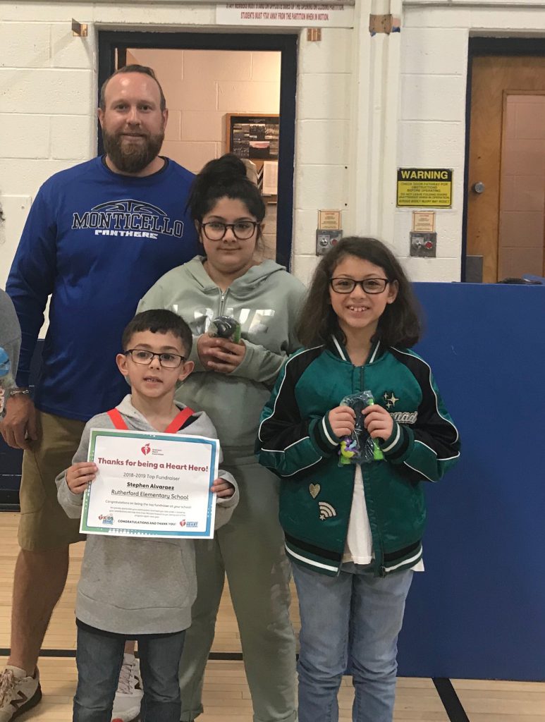 Man in blue shirt stands with three elementary students holding awards