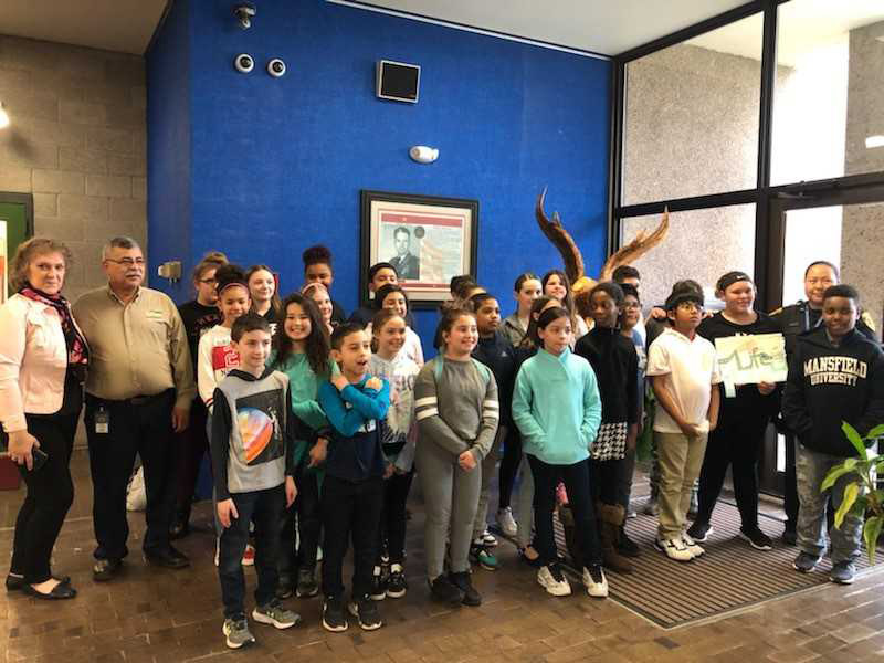 Group of about 30 fifth-grade students and three adults stand together. 