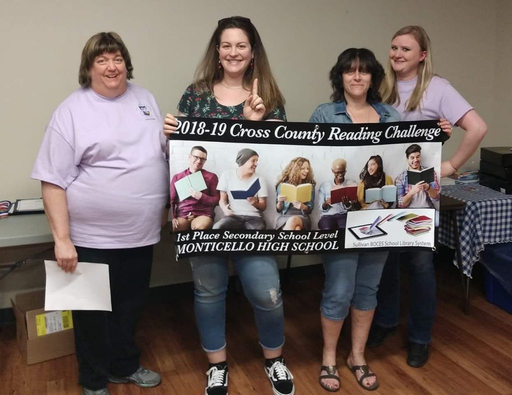 Four women, two holding a banner, declaring Monticello High School as the first place winner for secondary schools in reading in Sullivan County.