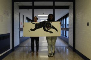 Two students stand in the hallway holding up a drawing of a Panther 