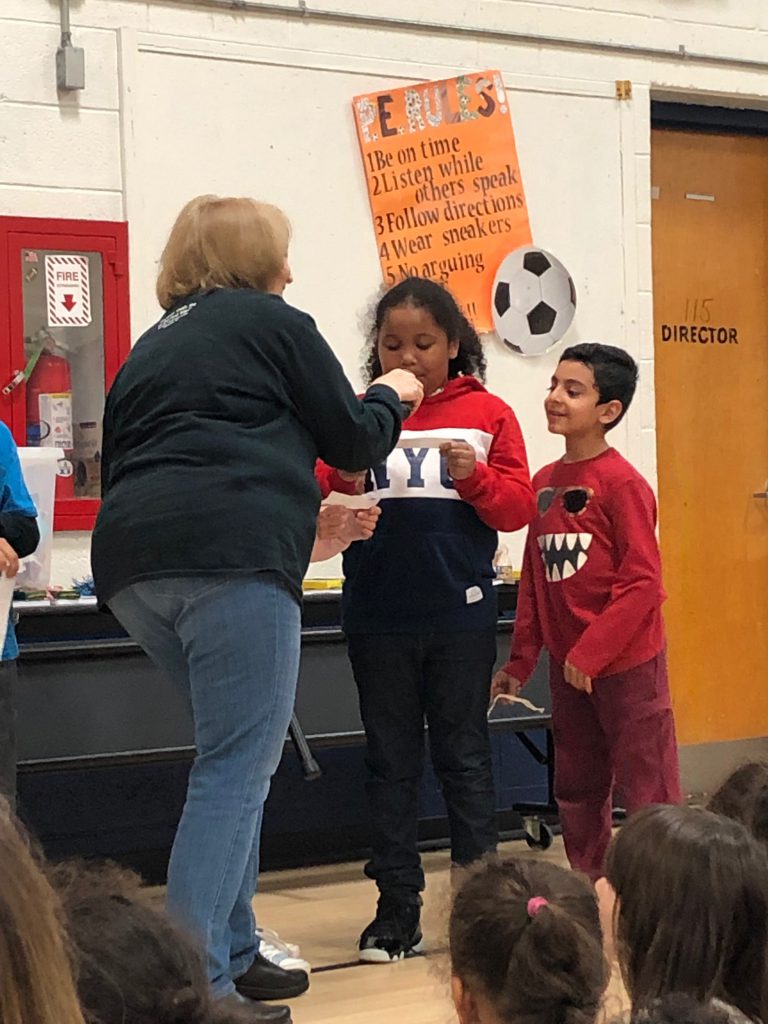 Female teacher gives awards to two elementary students each dressed in red shirts