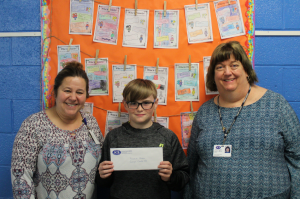 Monthly challenge winner Francis stands against a bulletin board holding his winning certificate