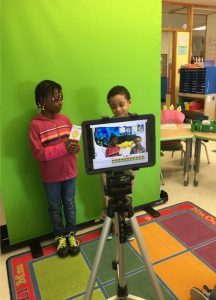 two students stand in front of the green screen 