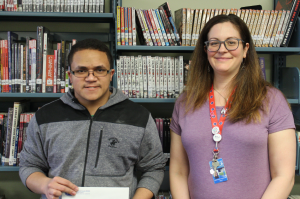 Student winner Ary stands in library holding prize 