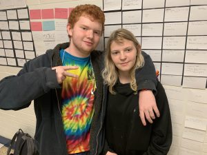 two students stand in front of the index cards that make up the wall of barriers