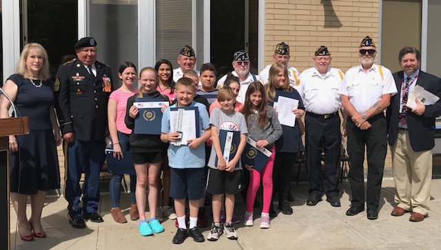 Ten fifth grade students stand with their awards surrounded by American Legion men in uniform and teachers.