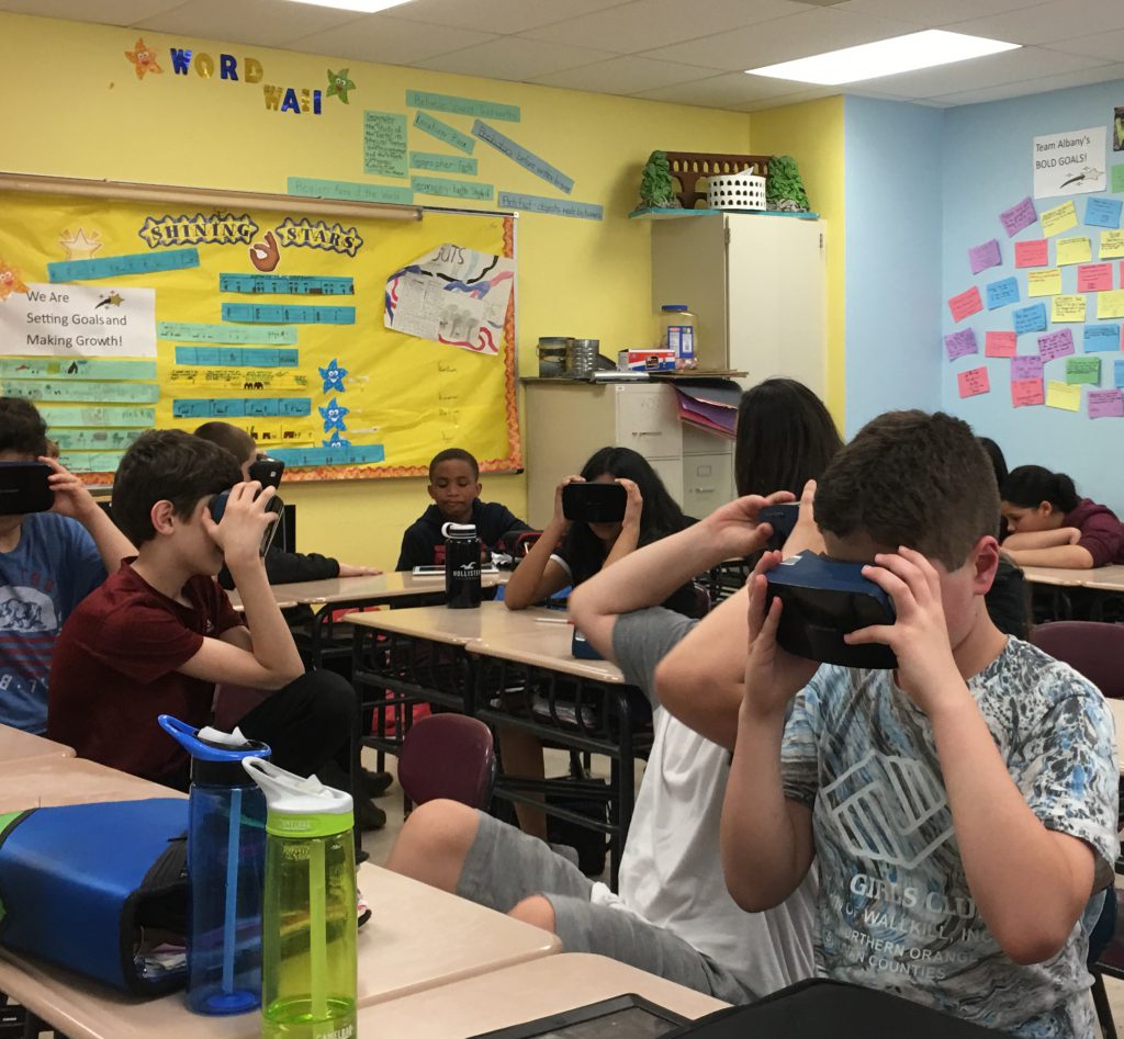 Several members of a middle school class holding virtual reality goggles to their eyes