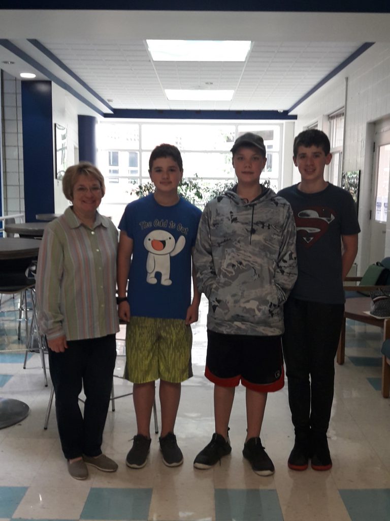 A woman at left standing next to three middle school boys