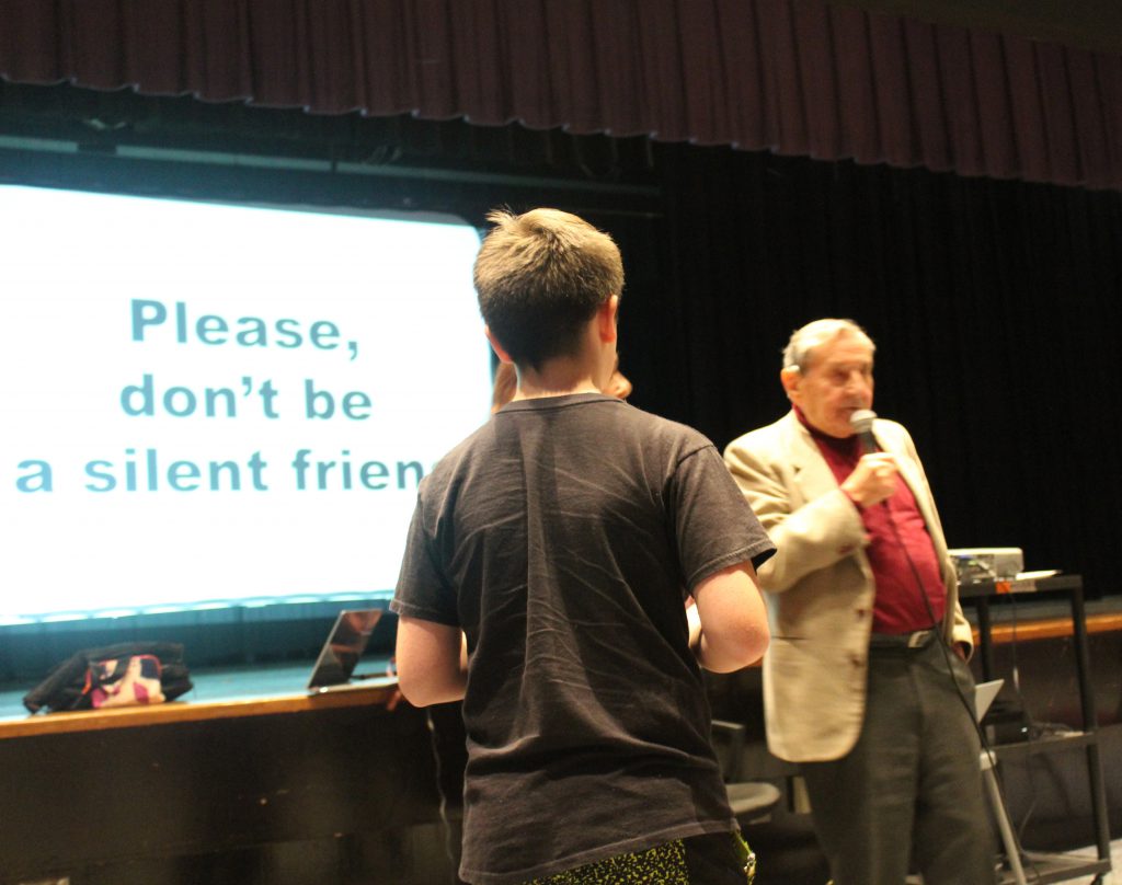 A student stands in front after asking a question. An elderly man holding a microphone answers it.