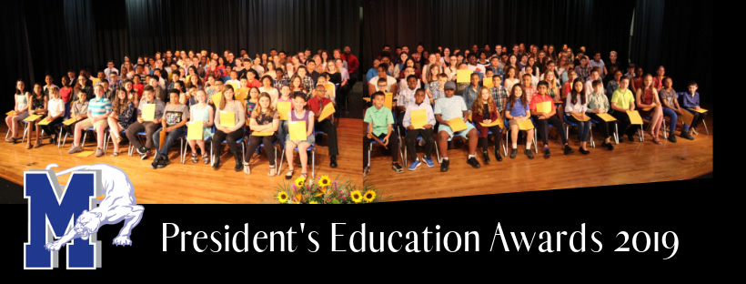 Hundreds of students sit on a stage holding their certificates.