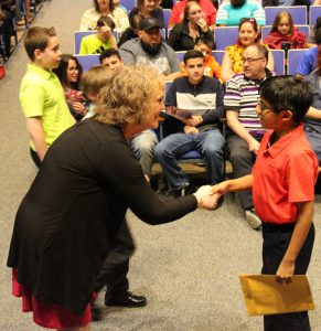 A woman in a black sweater leans down to shake the hand of a younger boy.