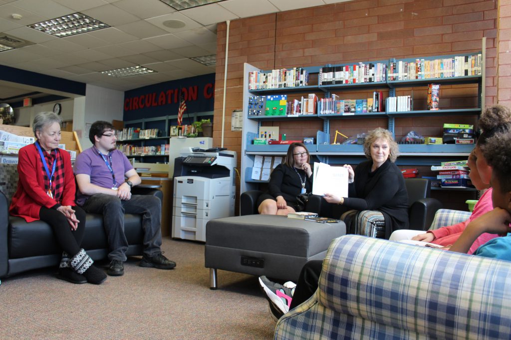 a group of students and adults sitting with a book around a table