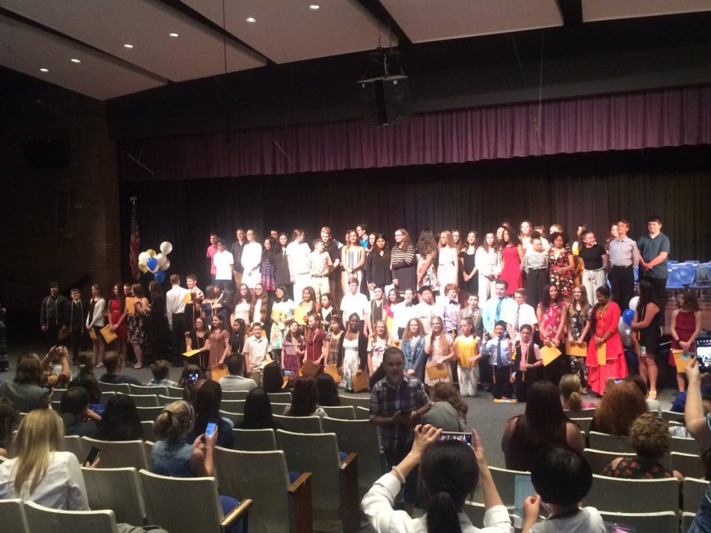 An auditorium filled with people and the stage is filled with middle school students 