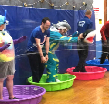 Five teachers stand in brightly colored wading pools as they are being squirted.