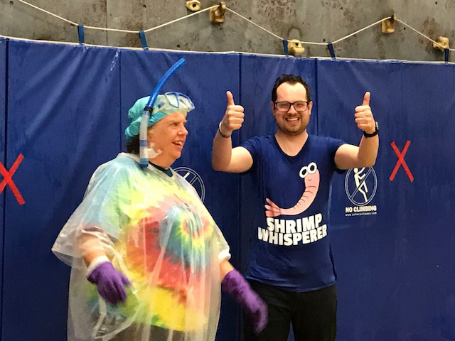 One staff member is wearing plastic to protect her from the water being squirted on her. Another teacher gives the thumbs up.