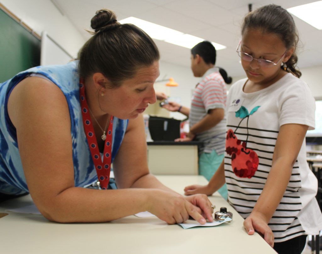 A woman with her hair pulled back in a bun shows a young girl the instructions for her lock.