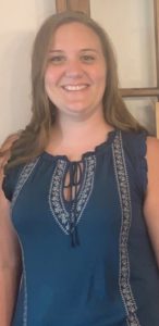 A woman with long brown hair, wearing a blue shirt is smiling