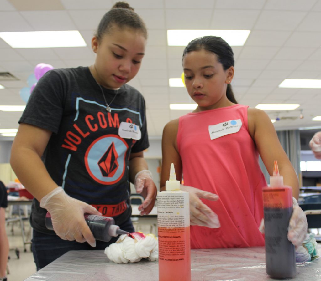 Two girls are using squirt bottles to tie-dye their t-shirts.