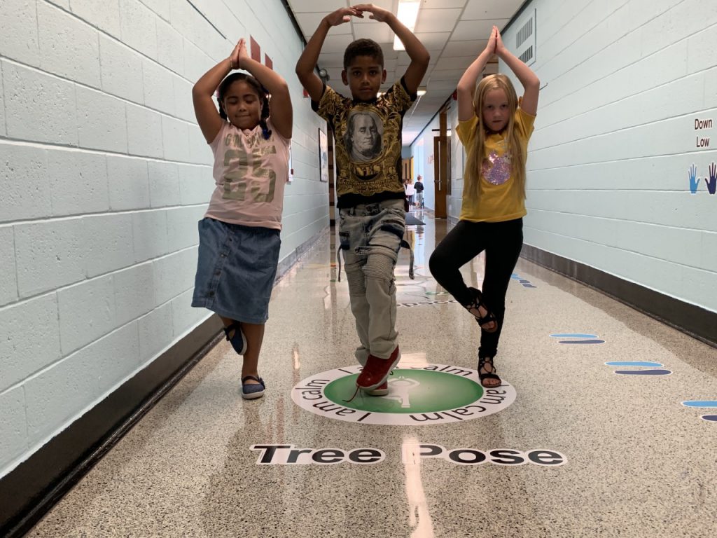 three students are standing in the yoga tree pose