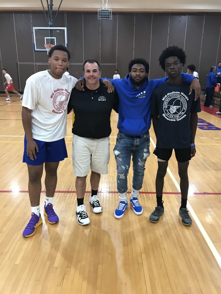 Three high school basketball players stand with their coach on a basketball court
