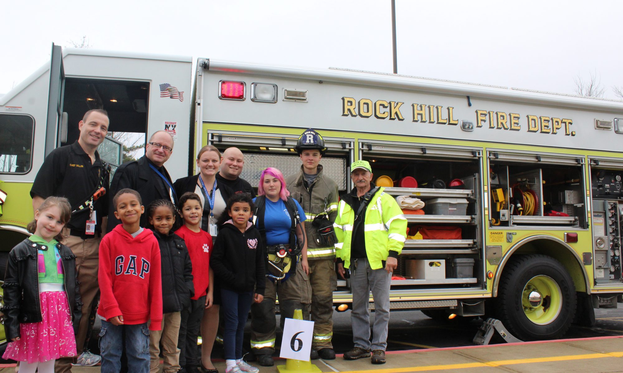 students, administrators and firefighters stand in front of a firetruck