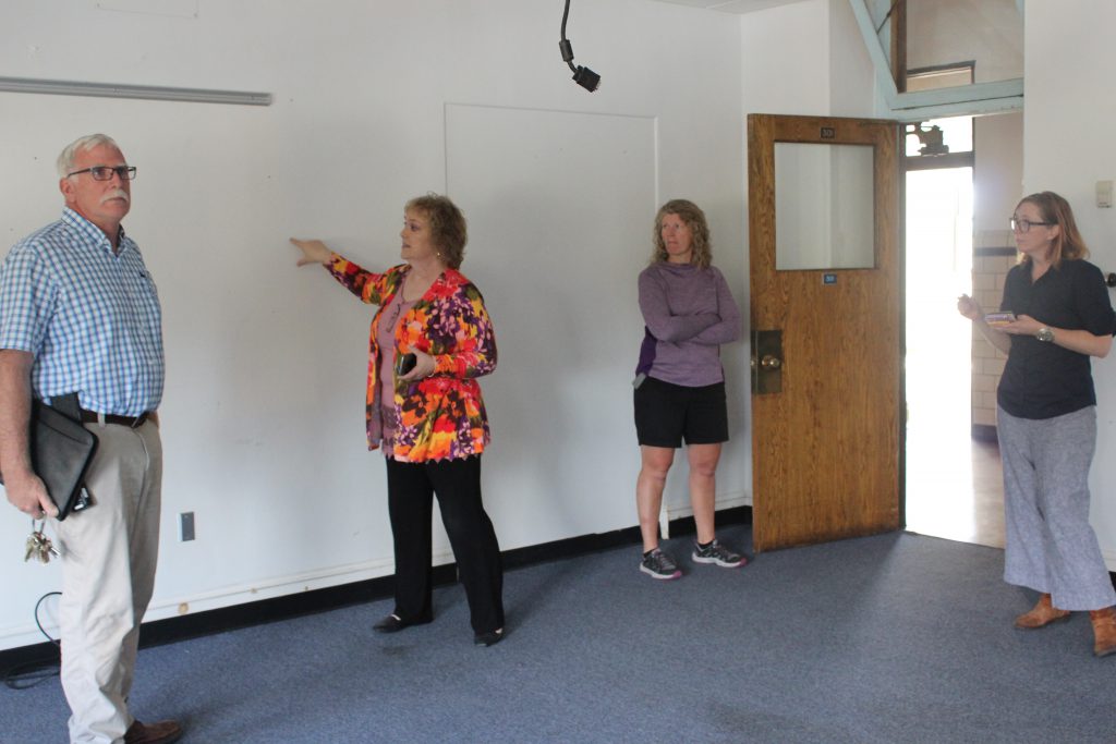 Board President Lori Orestano-James points to a wall while three other people look on 