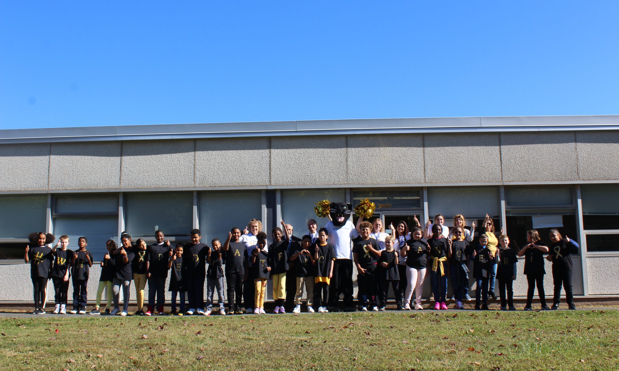 a large group of students are lined up by the school giving the "thumbs up" sign