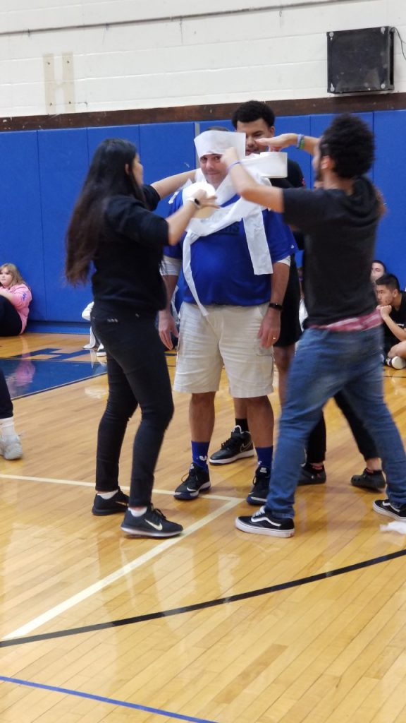 A group of four high school students wind toilet paper around a fellow student